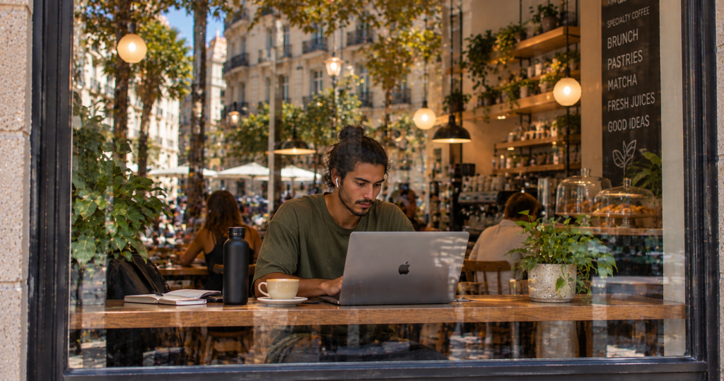 Chico trabajando con el portátil junto al ventanal de una cafetería en Madrid